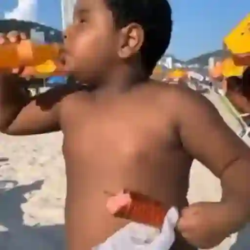 Figurinha: Criança bebendo suco na praia